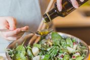 Nahaufnahme einer Hand die einen Salat mit Olivenöl verfeinert Nahaufnahme einer Hand die einen Salat mit Olivenöl verfeinert